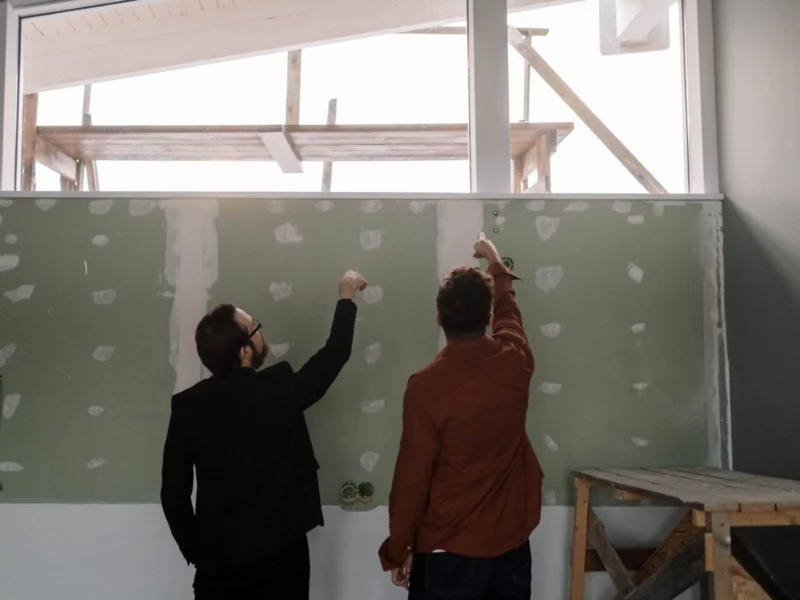 Deux personnes, de dos, font le point devant une cloison en plaques de plâtre sur un chantier